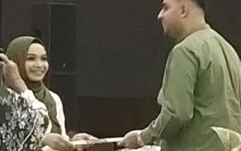 Dian Muhtadiah Hamna, M.Si. menyerahkan ijazah doktor kepada suaminya, Muhammad Awais. (Foto:MDA).